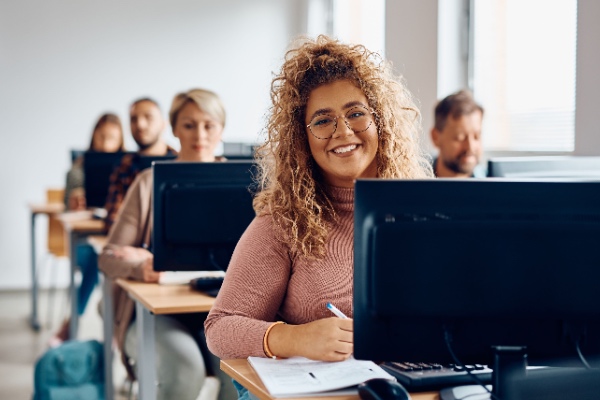 College student smiling at her computer in a classroom setting.