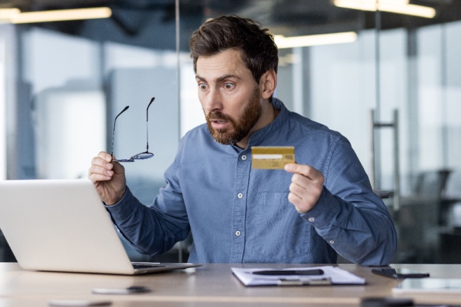 Man with shocked facial expression holding credit card