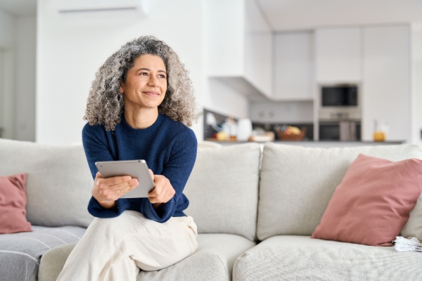 Mature woman sitting on couch with tablet in hand