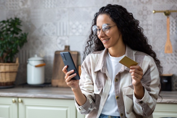 Woman sitting at home with cellphone and gift card in hand