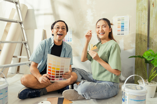 Father and daughter laughing in home with paint swatches in hand