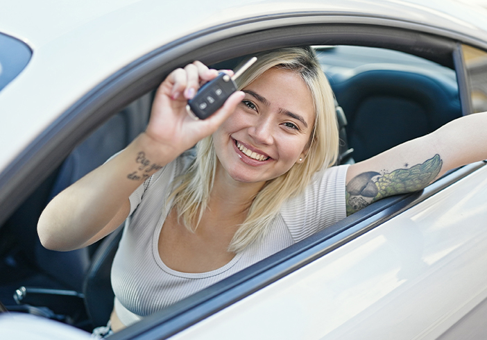 Woman sitting in a car with her arms out of the window holding a key fob