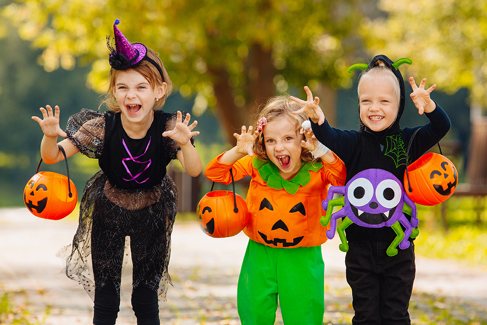 three happy kids walking on sidewalk wearing Halloween costumes