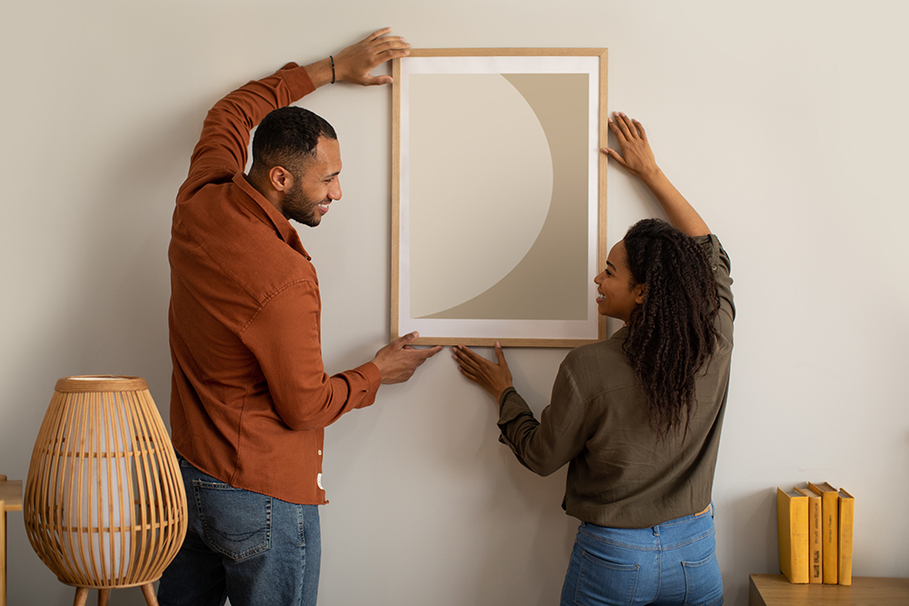 couple holding framed artwork up to the wall getting ready to hang it