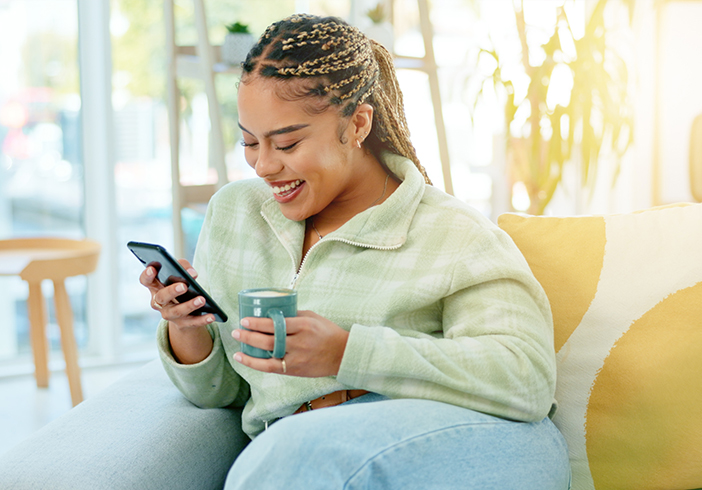 Woman sitting on a couch holding a phone and coffee mug