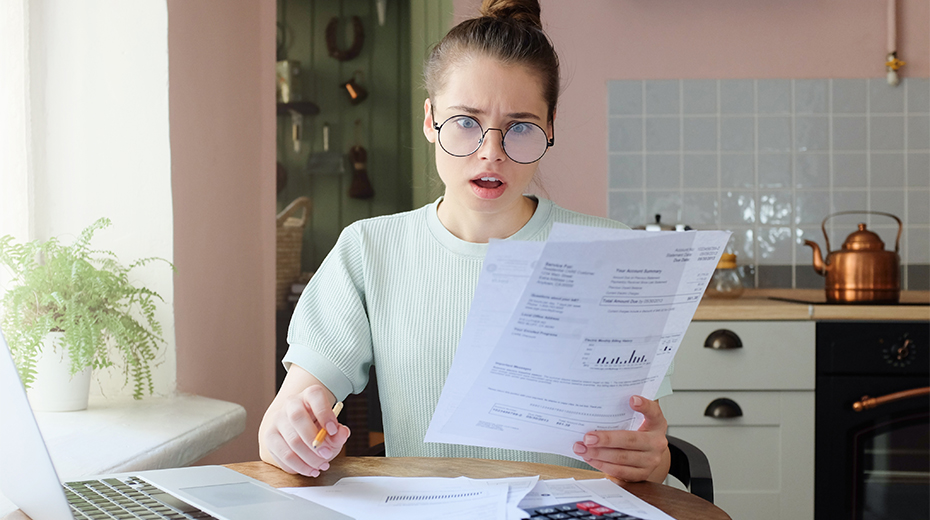 Woman sitting at kitchen table holding bill statements looking concerned